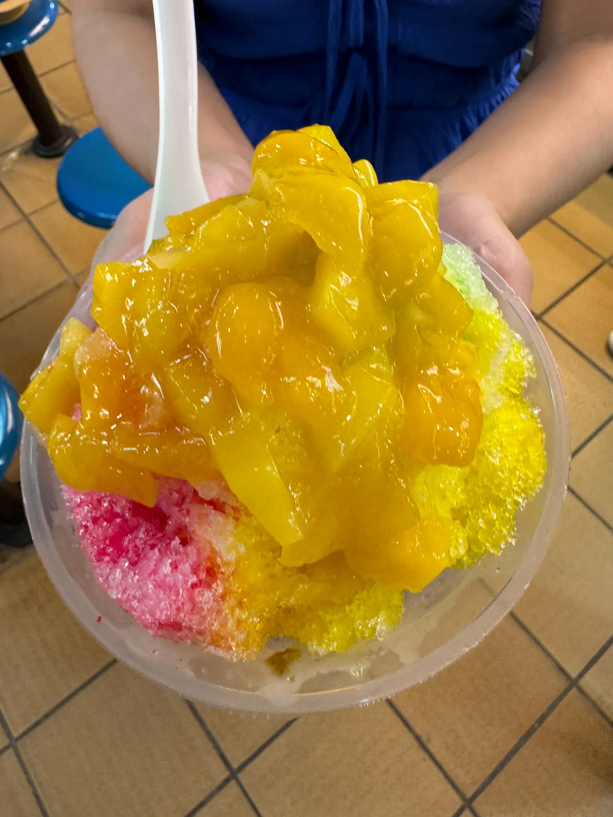 A bowl of ice kacang, rainbow shaved ice topped with mango, at a Singapore hawker center