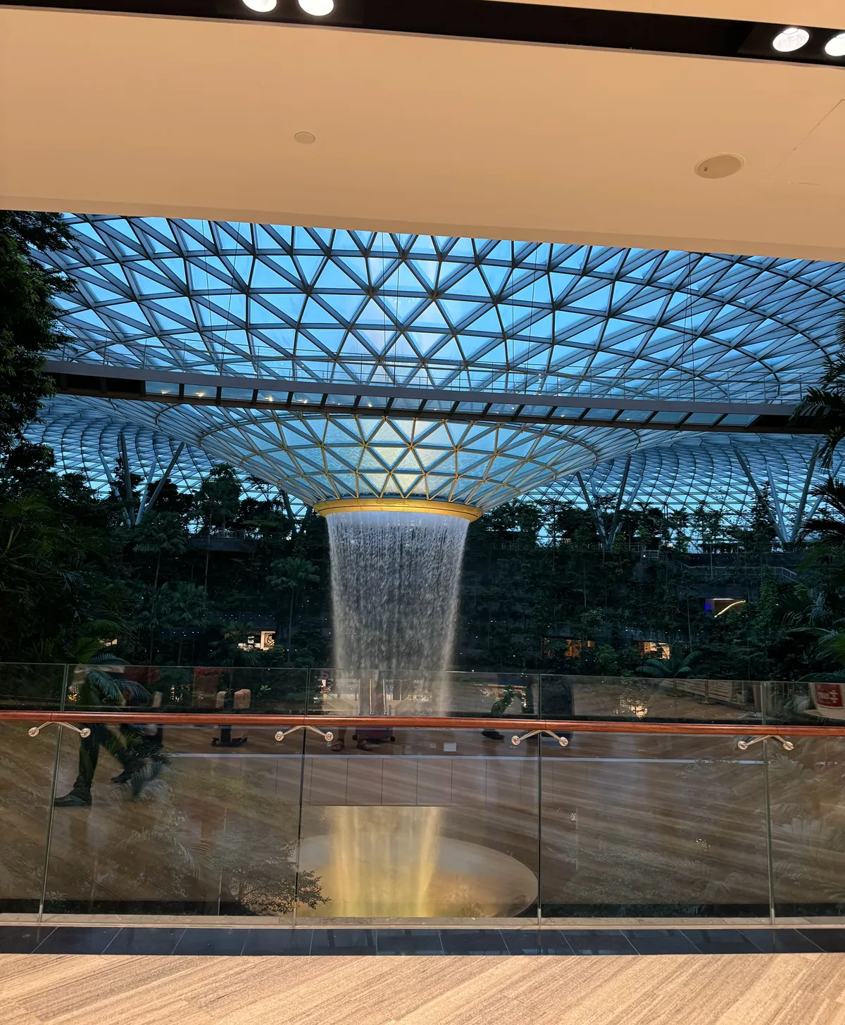 The Rain Vortex pouring from the glass dome at Jewel Changi Airport, surrounded by indoor forest
