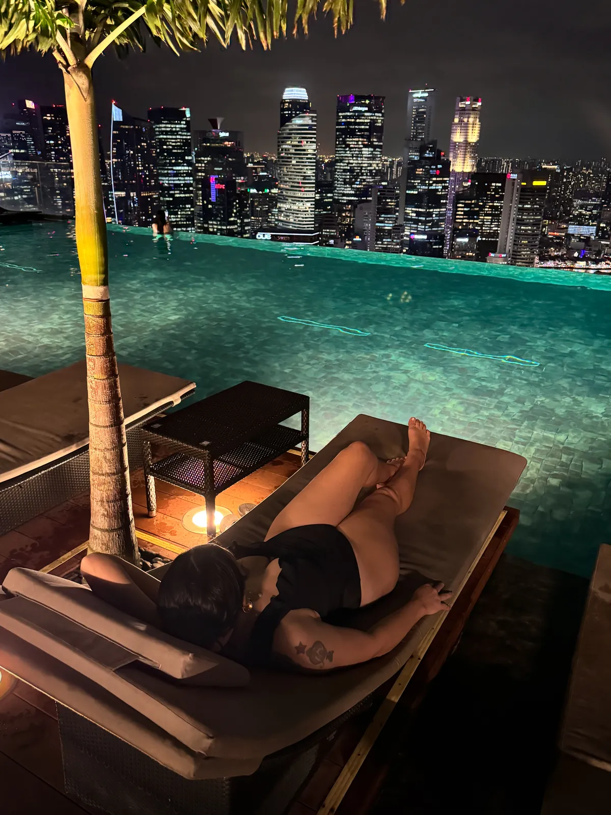 Liz lounging by the Marina Bay Sands Infinity Pool at night with the lit up Singapore skyline behind