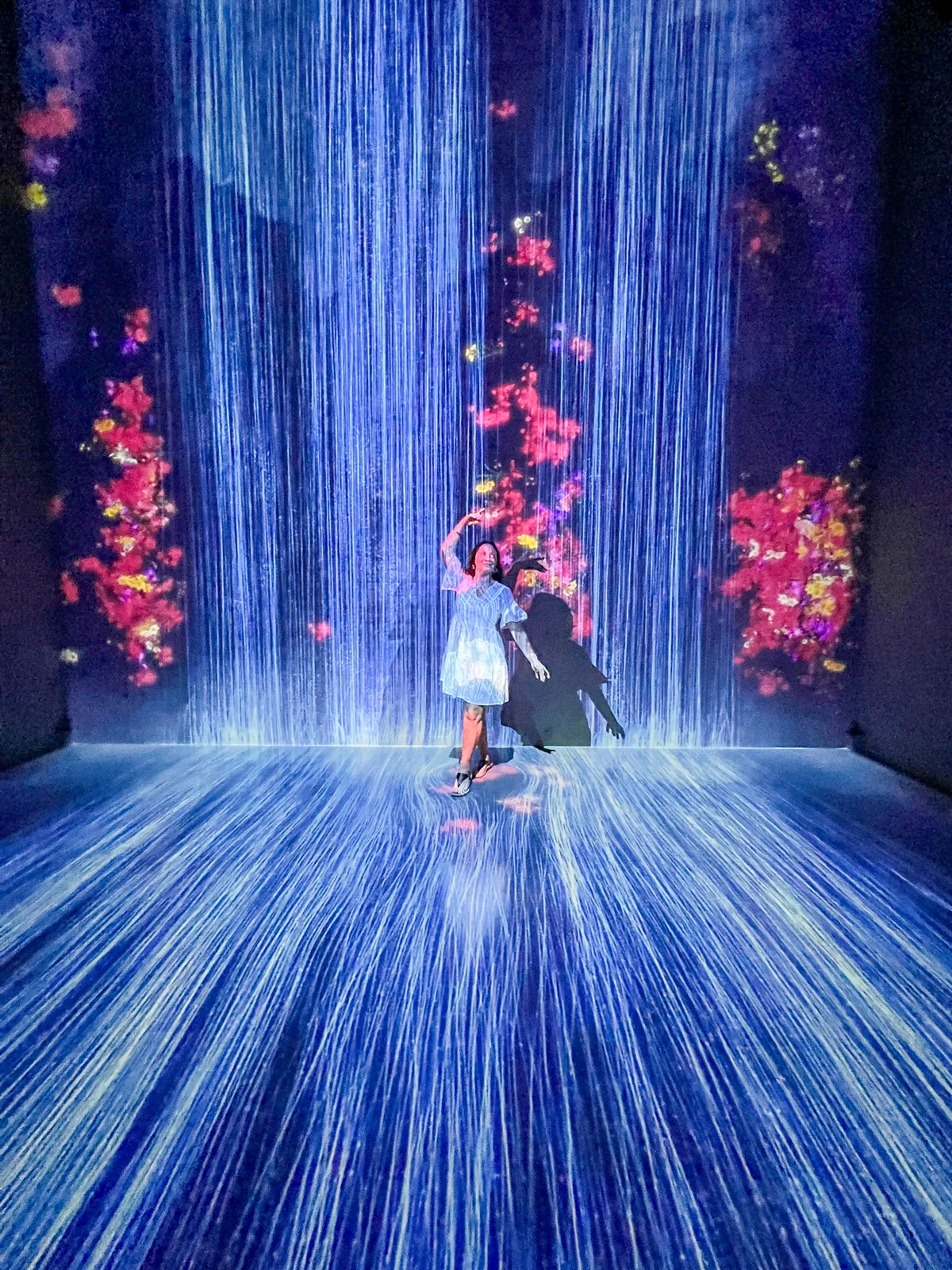 Liz posing in front of a digital waterfall with red flowers at teamLab Future World in Singapore