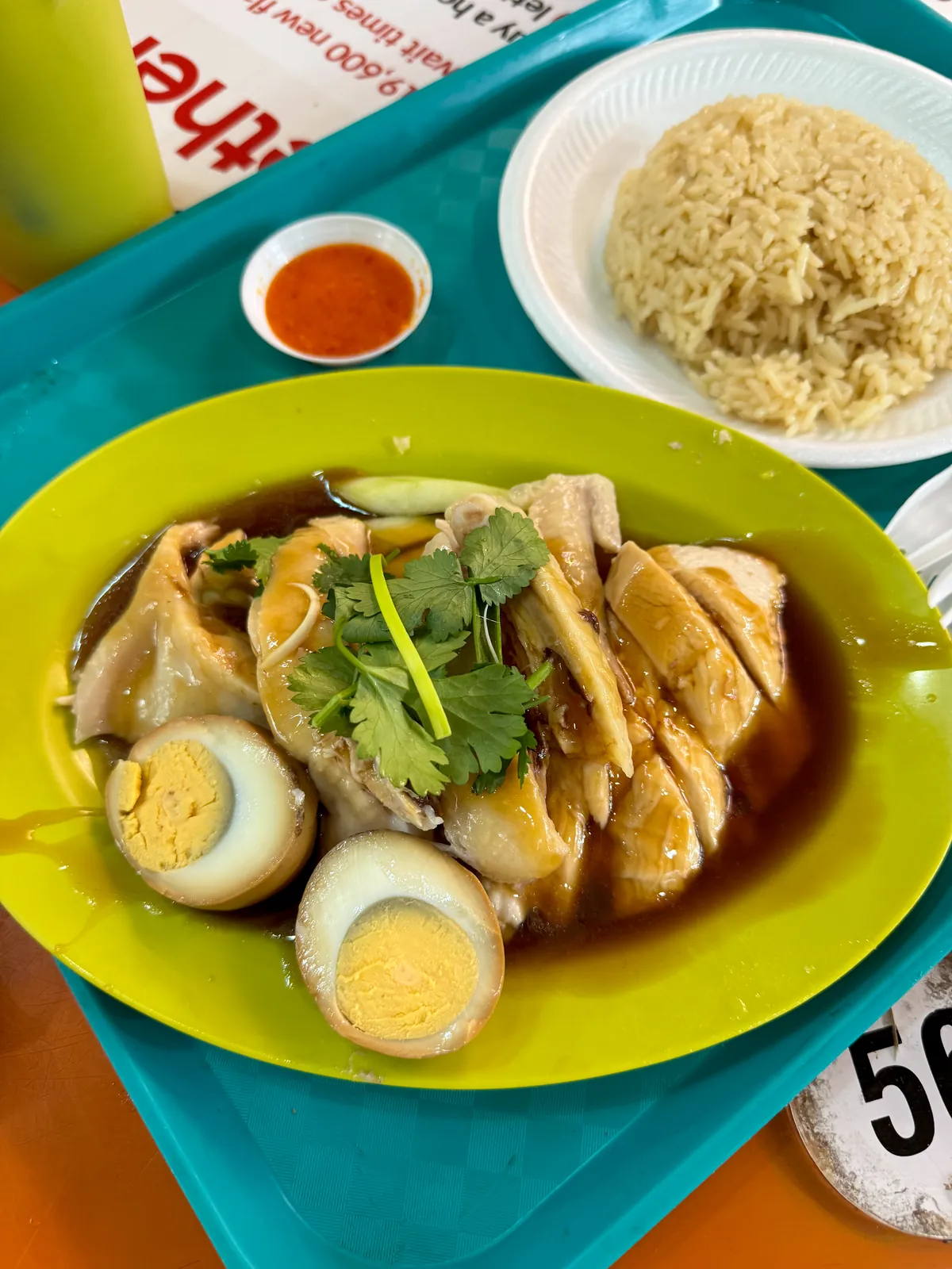 Plate of Hainanese chicken with braised eggs, rice and chili sauce at Maxwell Food Centre in Singapore