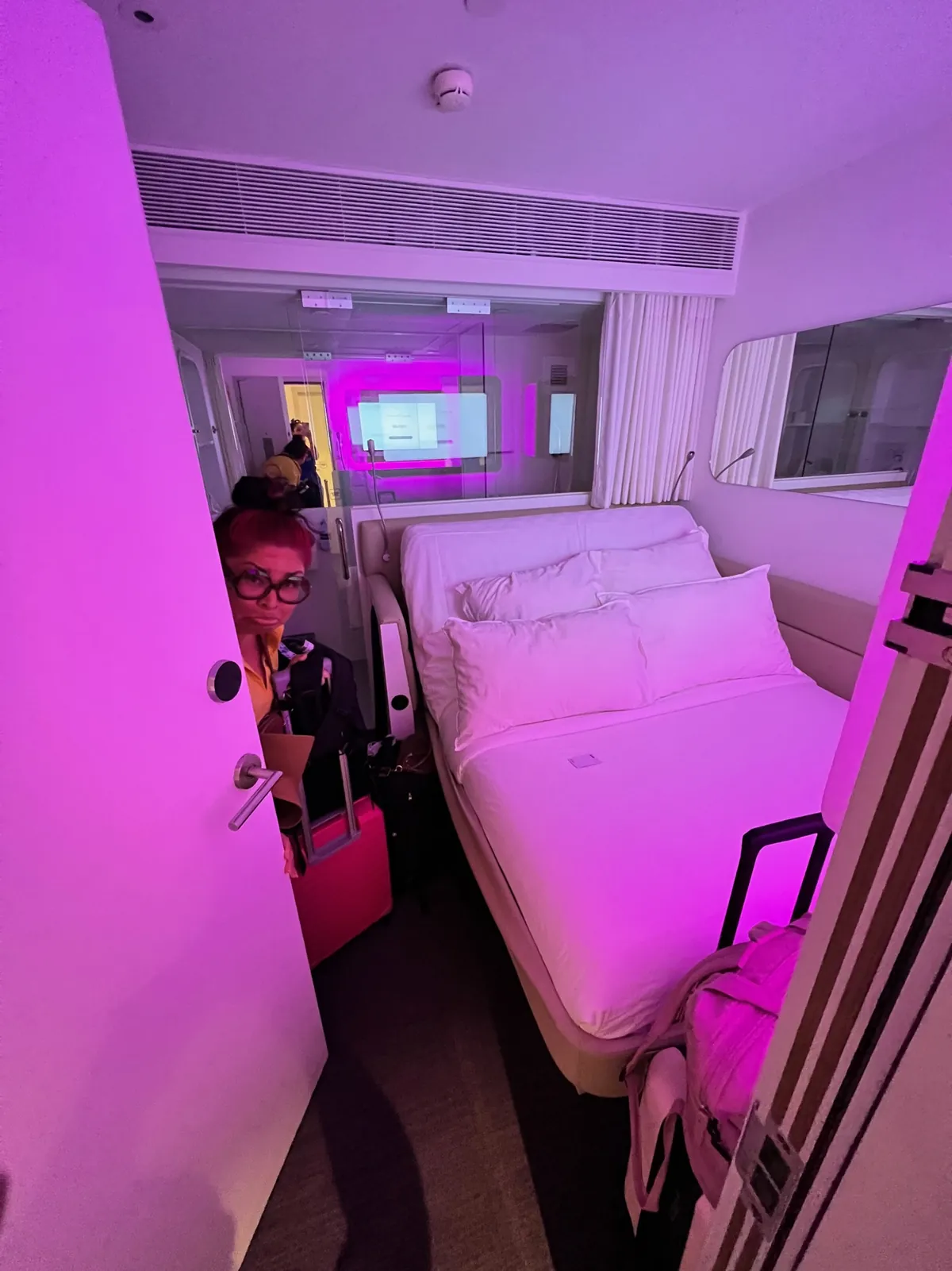 Cynthia at the door of a compact YOTELAIR cabin at Jewel Changi Airport, with the bed lit in pink and purple