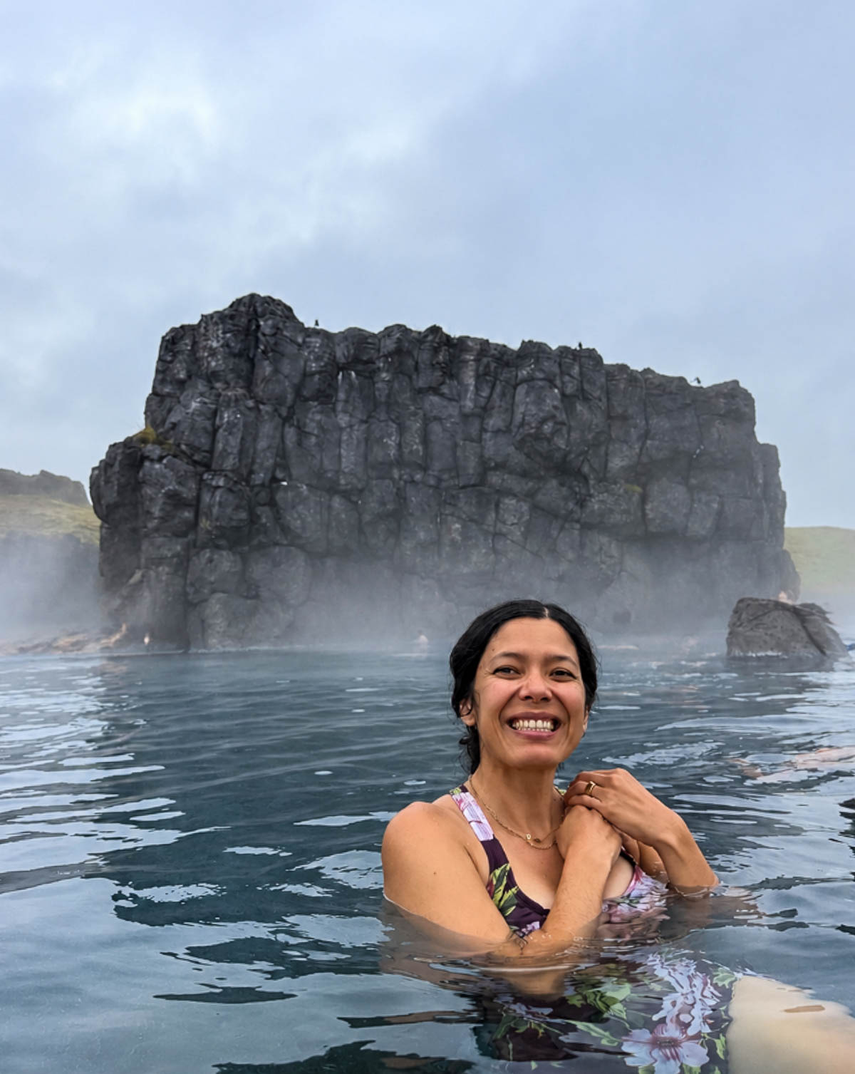 Toni smiling in the water at Sky Lagoon with a rock wall behind her