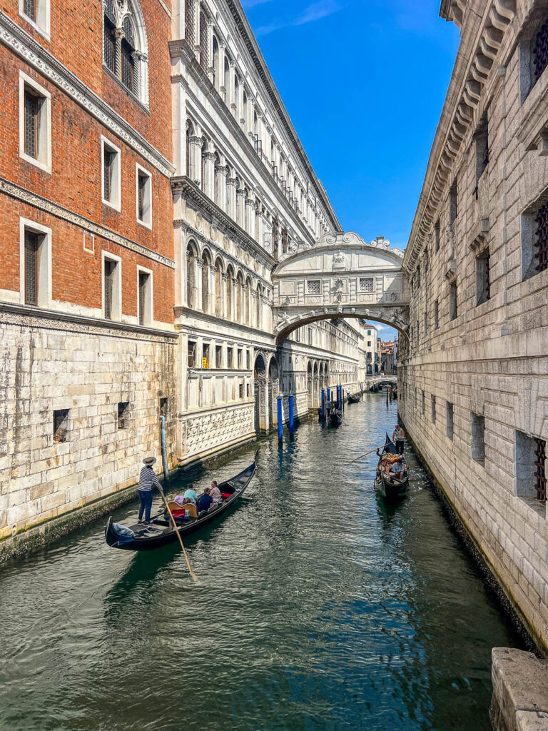 The enclosed white stone Bridge of Sighs over a narrow canal, with a gondola passing below.