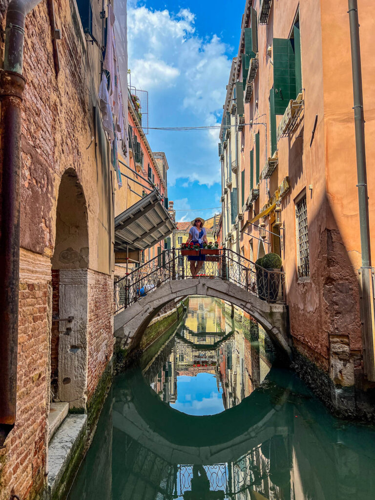 A small stone bridge reflected in the still water of a narrow Venice canal.