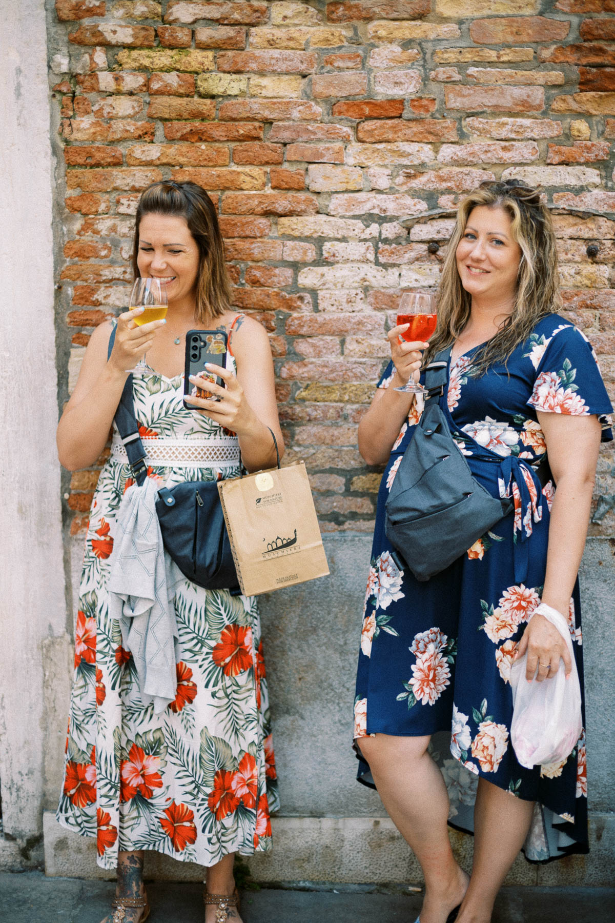 Two travelers holding spritzes in front of an old brick wall in Venice