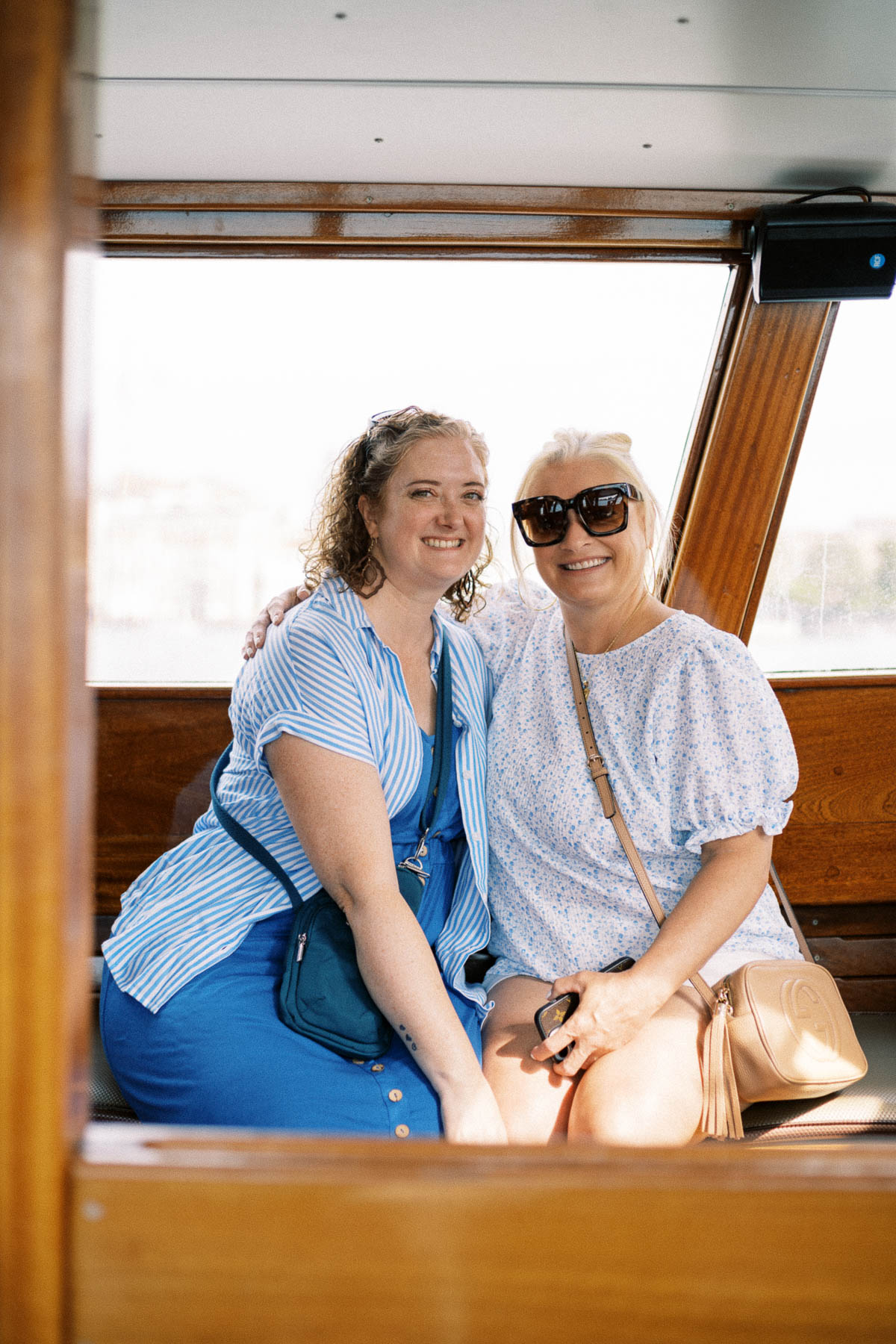 Two travelers smiling by the window of a water taxi in Venice